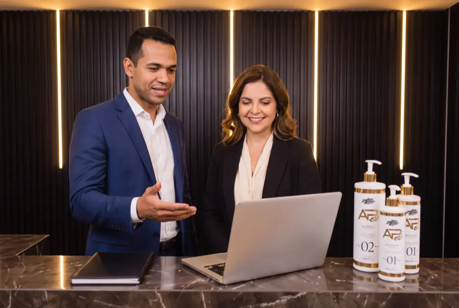 Distribuidor e dona do salão revisam os resultados no laptop, em visita de acompanhamento